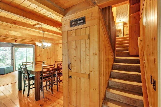 dining area with light hardwood / wood-style floors, beamed ceiling, wood ceiling, wood walls, and a chandelier