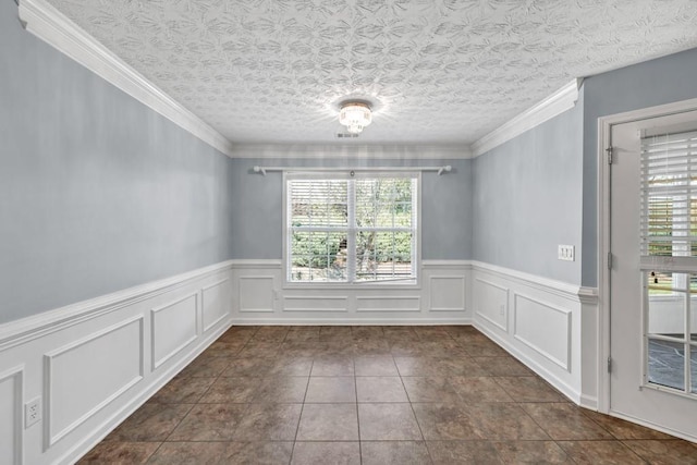 spare room featuring dark tile patterned floors, wainscoting, and crown molding