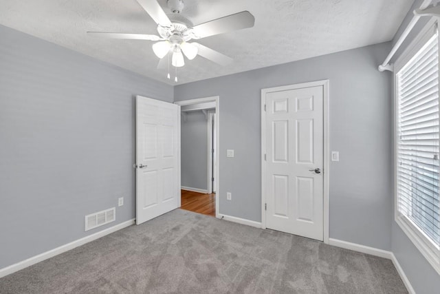 unfurnished bedroom with carpet floors, a textured ceiling, a ceiling fan, baseboards, and visible vents