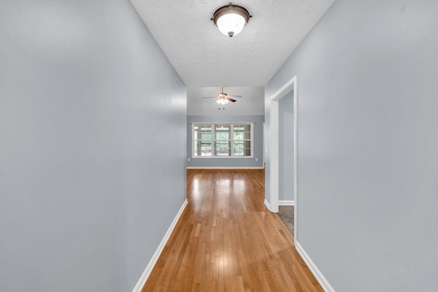 hallway featuring a textured ceiling, baseboards, and light wood finished floors