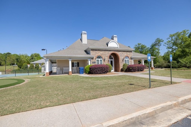 view of front of house with fence, covered porch, a front yard, roof with shingles, and a chimney