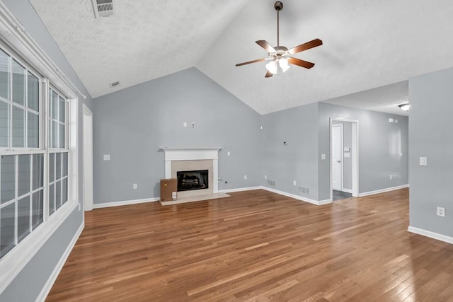 unfurnished living room featuring ceiling fan, a fireplace with flush hearth, wood finished floors, vaulted ceiling, and visible vents