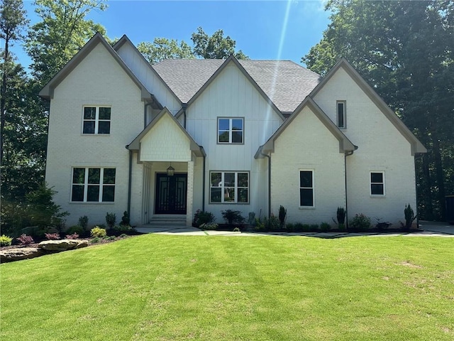 view of front facade with brick siding, board and batten siding, a front yard, and roof with shingles