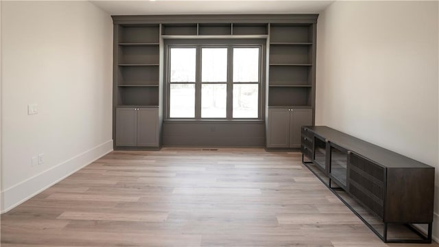 interior space featuring light wood-style flooring, built in shelves, and baseboards