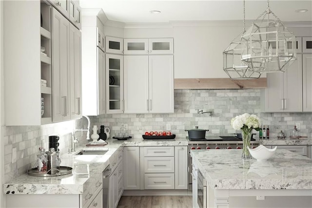 kitchen featuring a sink, glass insert cabinets, light stone counters, and crown molding