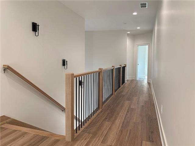 corridor with wood finished floors, visible vents, baseboards, recessed lighting, and an upstairs landing