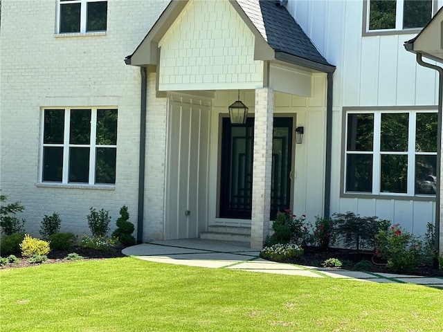 property entrance featuring brick siding, a lawn, board and batten siding, and roof with shingles