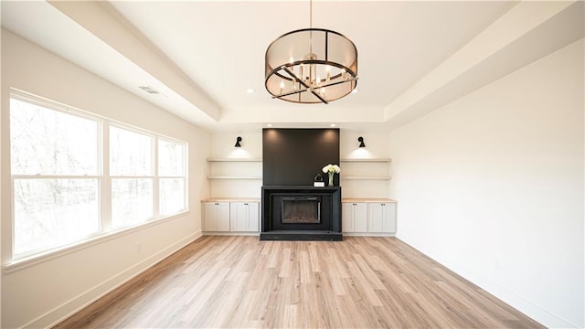 unfurnished living room with baseboards, light wood finished floors, a tray ceiling, a fireplace, and a notable chandelier