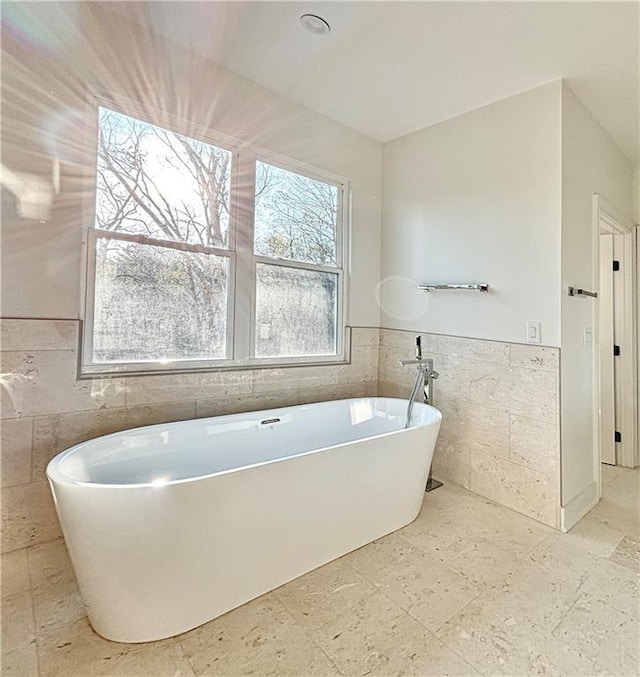 full bath featuring a soaking tub, tile walls, and a wainscoted wall