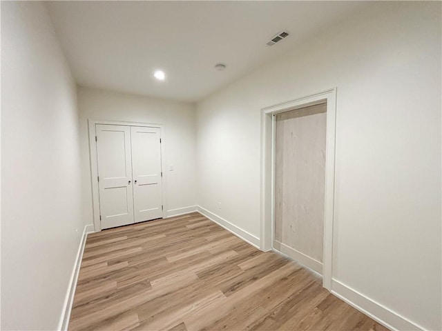 spare room featuring light wood finished floors, visible vents, and baseboards