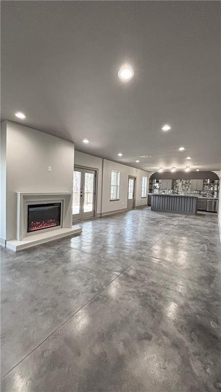 unfurnished living room featuring recessed lighting, baseboards, a lit fireplace, and concrete flooring