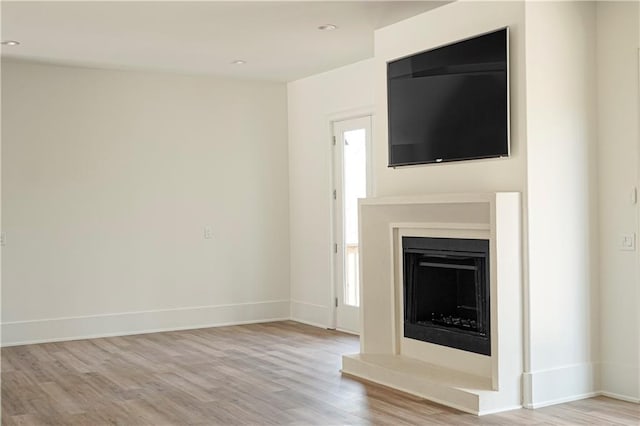 unfurnished living room featuring recessed lighting, baseboards, a fireplace with raised hearth, and wood finished floors