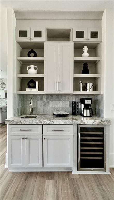 bar featuring beverage cooler, backsplash, light wood-style floors, and a sink