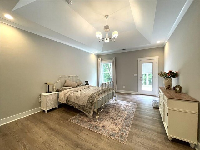 bedroom featuring an inviting chandelier, a raised ceiling, hardwood / wood-style floors, and access to exterior