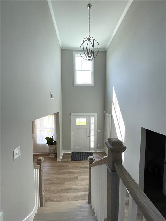 entryway with light wood-type flooring, ornamental molding, a notable chandelier, and plenty of natural light