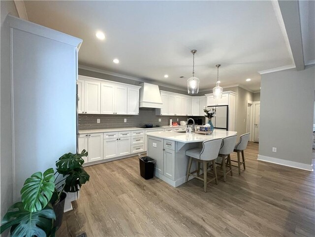 kitchen with white refrigerator, hardwood / wood-style flooring, white cabinetry, custom exhaust hood, and a center island with sink