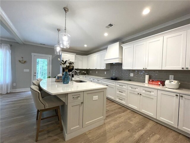 kitchen with white cabinets, custom exhaust hood, decorative light fixtures, a kitchen island with sink, and sink