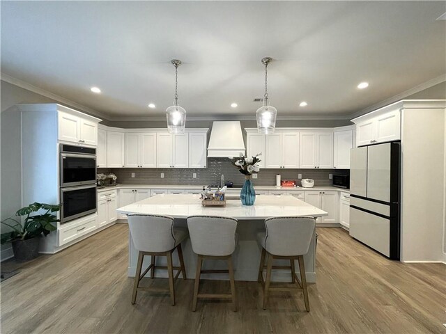 kitchen with custom range hood, pendant lighting, stainless steel double oven, hardwood / wood-style flooring, and refrigerator