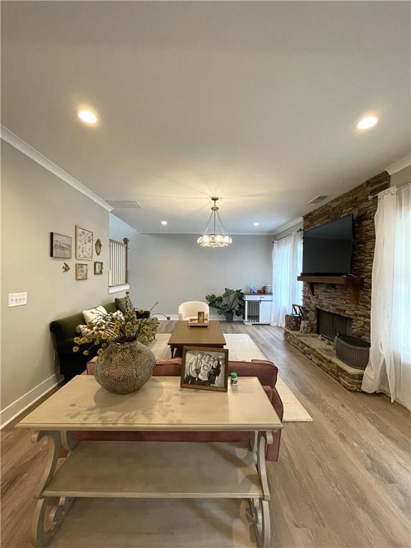 dining room featuring light hardwood / wood-style floors, crown molding, a stone fireplace, and an inviting chandelier