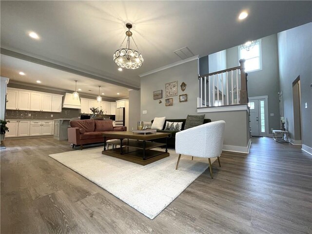 living room with an inviting chandelier, hardwood / wood-style flooring, a towering ceiling, and ornamental molding