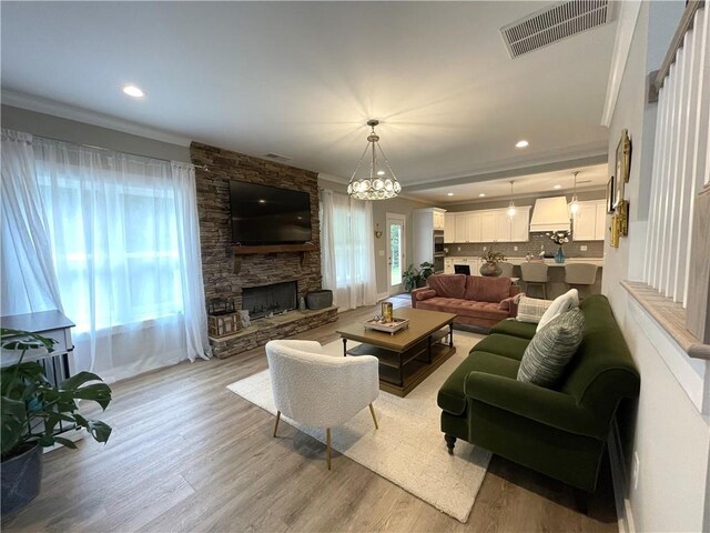 living room with a stone fireplace, a notable chandelier, light hardwood / wood-style floors, and a wealth of natural light