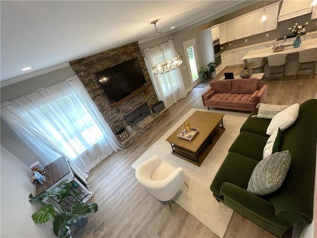 living room featuring an inviting chandelier, light hardwood / wood-style flooring, and a stone fireplace