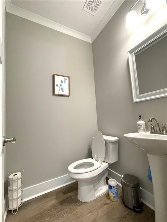 bathroom featuring wood-type flooring, ornamental molding, and toilet