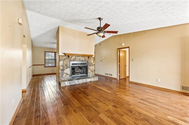 unfurnished living room featuring a stone fireplace, ceiling fan, a textured ceiling, vaulted ceiling, and light hardwood / wood-style flooring