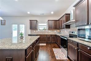 kitchen featuring light stone countertops, a center island, dark wood-type flooring, stainless steel appliances, and wall chimney range hood