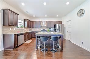 kitchen with wall chimney range hood, dark hardwood / wood-style floors, a breakfast bar, a kitchen island, and appliances with stainless steel finishes