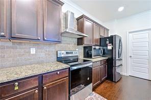 kitchen featuring light stone countertops, appliances with stainless steel finishes, dark brown cabinets, wall chimney range hood, and dark hardwood / wood-style floors