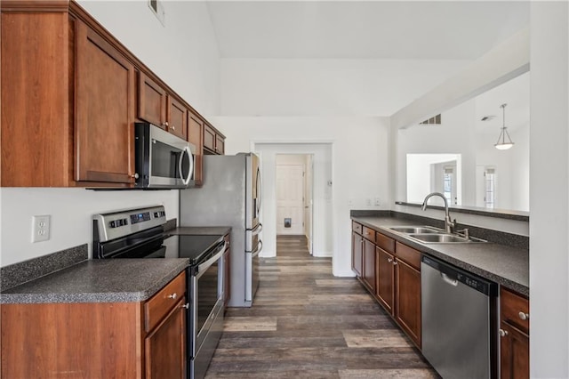 kitchen featuring dark wood-style flooring, a sink, appliances with stainless steel finishes, brown cabinets, and dark countertops