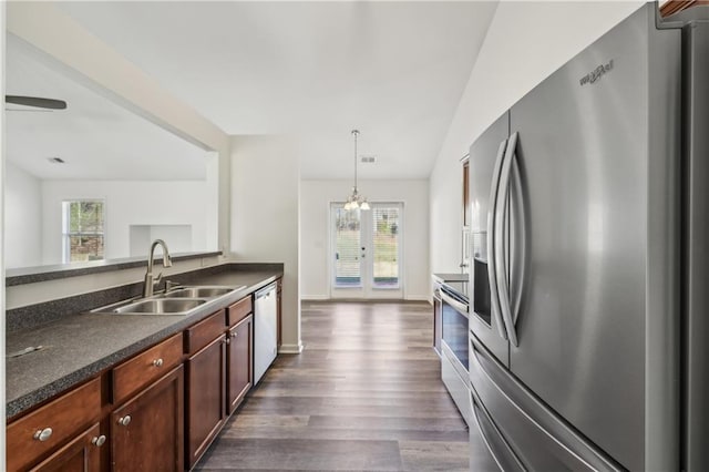 kitchen with dark wood-style flooring, stainless steel appliances, dark countertops, hanging light fixtures, and a sink