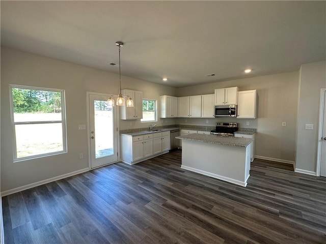 kitchen with light stone counters, decorative light fixtures, a kitchen island, stainless steel appliances, and white cabinets