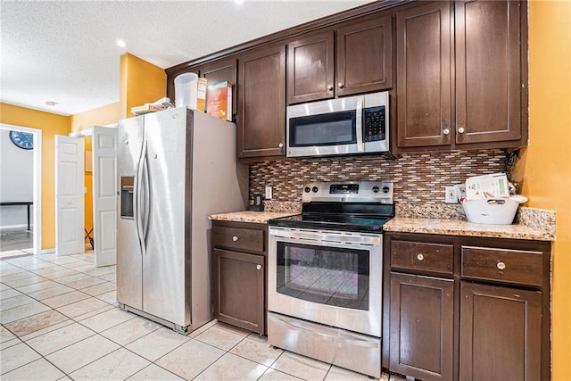 kitchen featuring stainless steel appliances, tasteful backsplash, dark brown cabinetry, light tile patterned flooring, and a textured ceiling