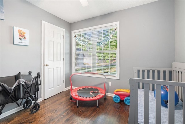 bedroom with baseboards, wood finished floors, a crib, and a ceiling fan