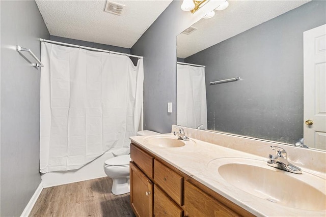 full bath with wood finished floors, double vanity, toilet, shower / bath combo with shower curtain, and a textured ceiling