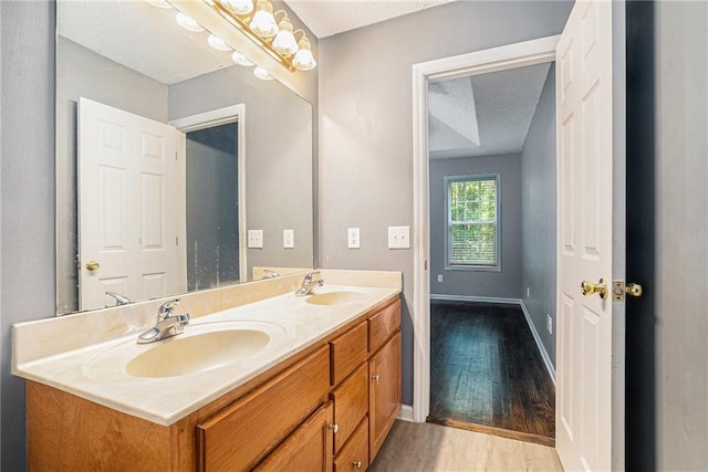 bathroom featuring wood finished floors, a textured ceiling, double vanity, and baseboards