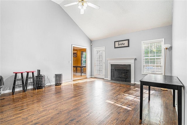 unfurnished living room featuring a ceiling fan, wood finished floors, high vaulted ceiling, a fireplace with raised hearth, and baseboards