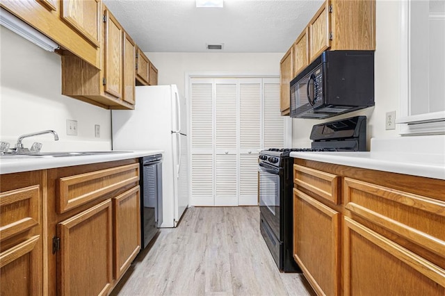 kitchen with a sink, visible vents, light wood-type flooring, brown cabinets, and black appliances