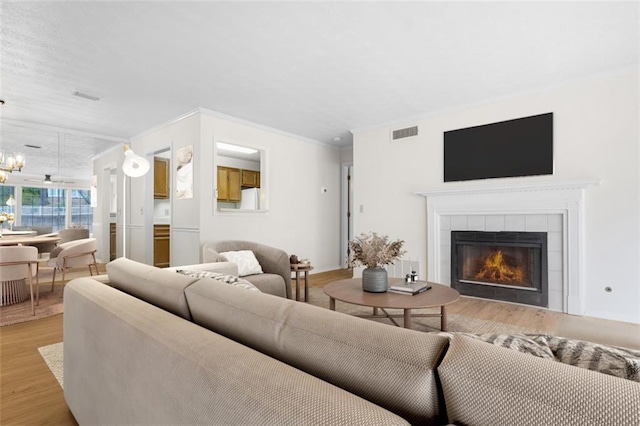 living room featuring light wood finished floors, visible vents, a tile fireplace, ornamental molding, and a notable chandelier