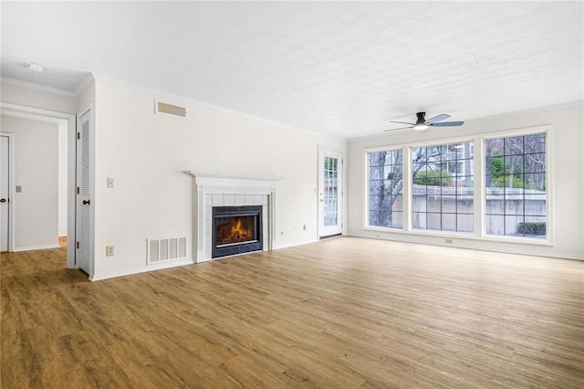 unfurnished living room featuring ornamental molding, wood finished floors, a tile fireplace, and visible vents