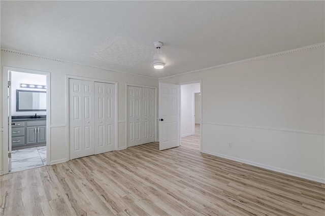 7020 Camp Valley Rd, Riverdale, GA 30296 - unfurnished bedroom with multiple closets, baseboards, connected bathroom, a sink, and light wood-style flooring