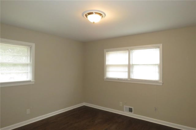 spare room featuring visible vents, baseboards, and dark wood-style flooring