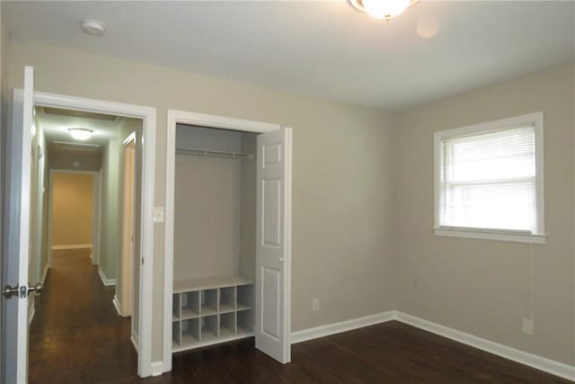 unfurnished bedroom with dark wood finished floors, baseboards, and a closet