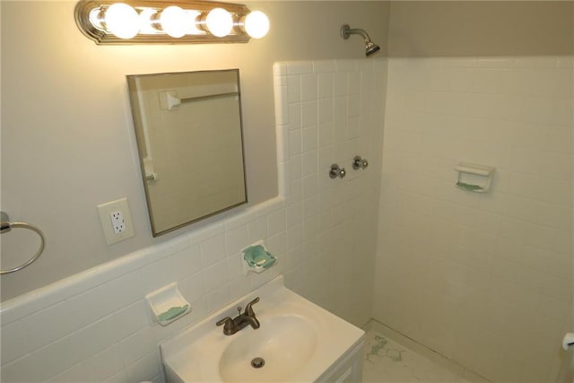 bathroom with tiled shower, tile walls, wainscoting, and vanity