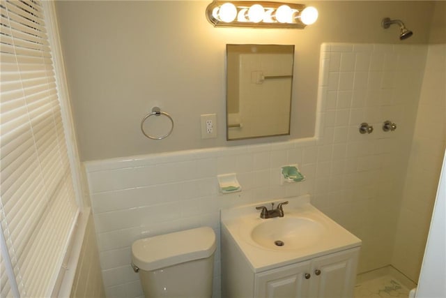 full bathroom featuring a wainscoted wall, toilet, a tile shower, tile walls, and vanity