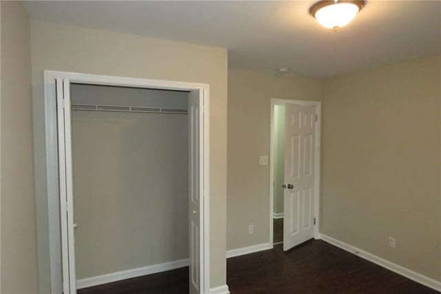 unfurnished bedroom featuring a closet, baseboards, and dark wood-style flooring