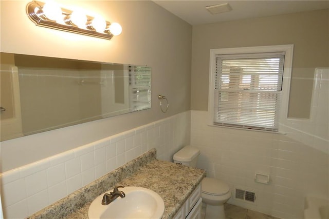 full bath featuring vanity, a wainscoted wall, visible vents, tile walls, and toilet