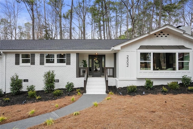 view of front facade with aphalt driveway, a shingled roof, brick siding, crawl space, and board and batten siding